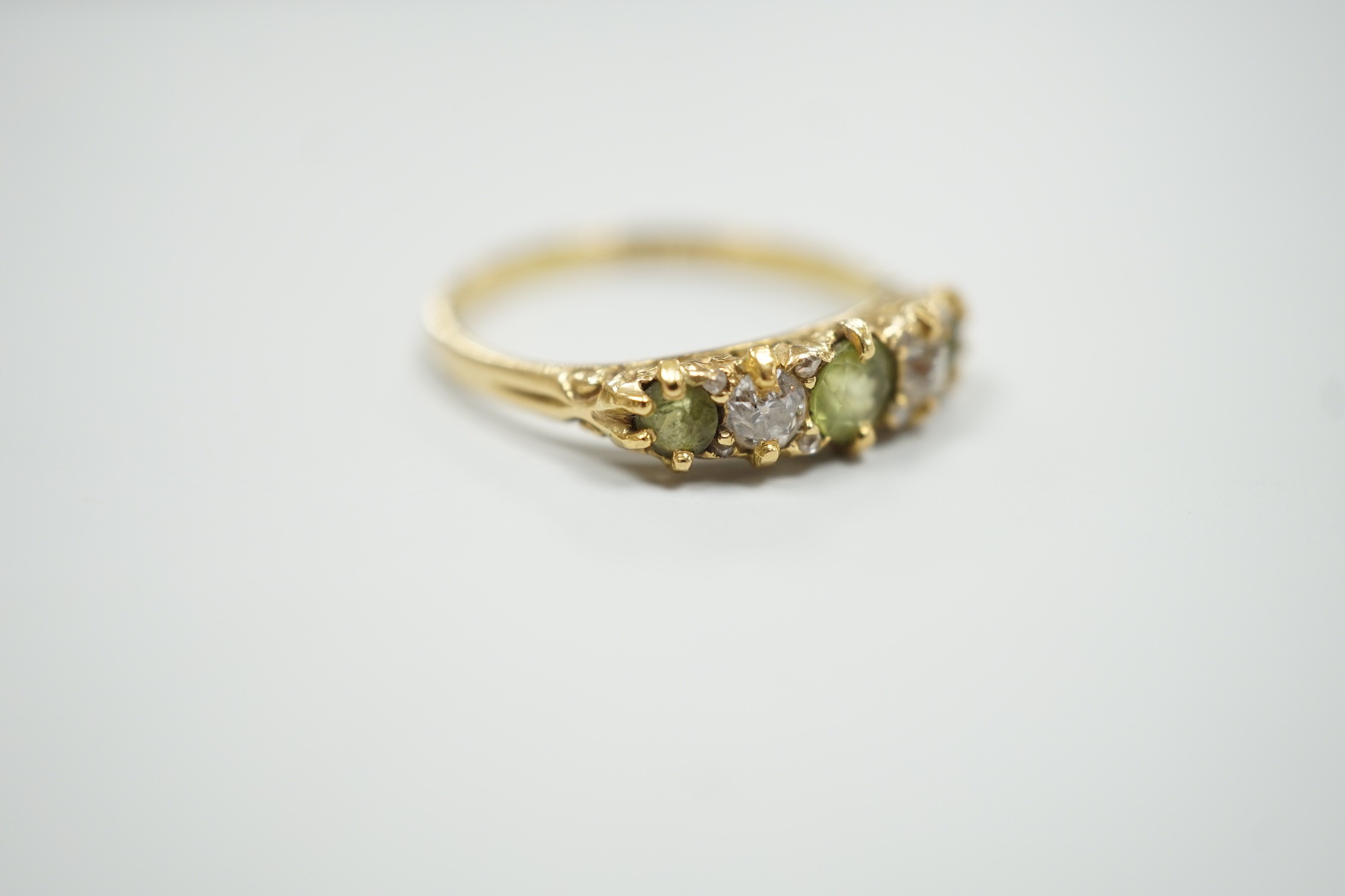An 18ct, three stone peridot and two stone diamond set half hoop ring. size N, gross weight 2.6 grams.